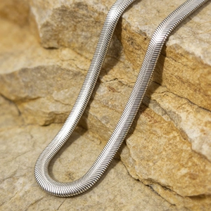 Collier minimaliste en maille serpent argentée sur un fond de roche texturée