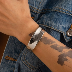 Bracciale rigido in metallo argento lucido indossato al polso con outfit in denim street