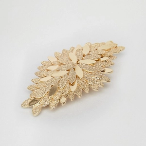 Detailed close-up of a golden spring hair clip with layered leaf patterns and glitter finish
