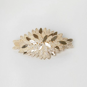 Detailed view of golden leaf-shaped spring hair clip with polished and matte textured layers