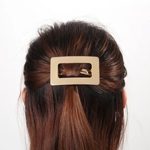 Macro detail of a matte gold rectangular hollow hair clip on brown hair