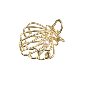 Detail view of a golden shell hair claw clip with cutout lines and a white pearl accent