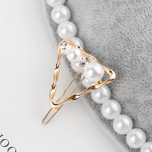 Macro detail of geometric triangular gold hair clip with large white pearls and crystals