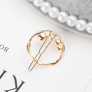 Detail of round golden hair clip with embedded white pearls on minimalist alloy frame