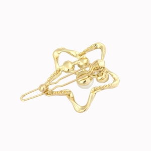 Detailed macro shot of a geometric wavy gold star hair clip with small pearl accents