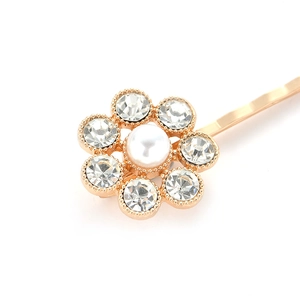Close-up of golden floral hair clip with clear rhinestones and white pearl center