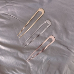 Macro detail of three U-shaped hairpins in gold, silver, and rose gold on silk