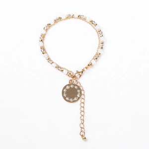 Close-up of double-layer beaded gold bracelet with a crystal-encrusted disc pendant