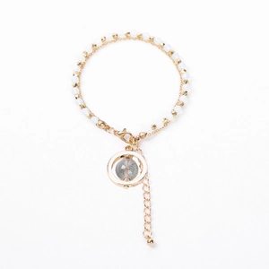 Detail view of a double-layered gold beaded bracelet with blue stone pendant and lobster clasp