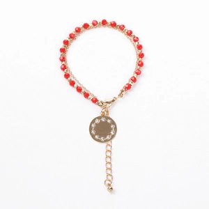 Detail of red beaded and gold chain bracelet featuring a sparkling zircon round pendant