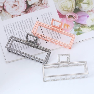 Three geometric hollow metal hair claws in rose gold, gun black, and silver on a floral book