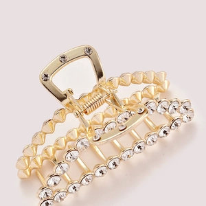 Detail of a large gold metal hair claw clip featuring sparkling rhinestone embellishments