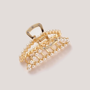 Detail of a golden metal hair claw clip with glossy pearls and sparkling rhinestones