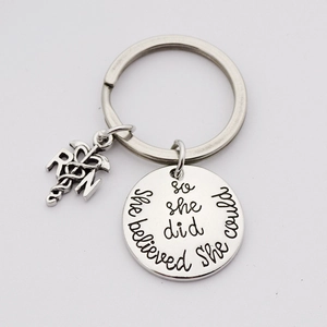 Detail of silver nurse keychain with caduceus charm and she believed quote engraving