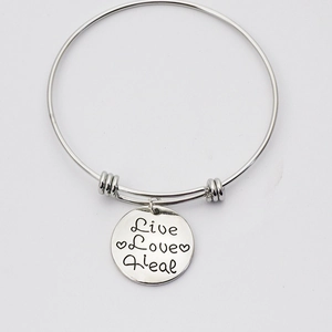 Macro shot of silver metal bangle featuring a round tag with Live Love Heal engraving