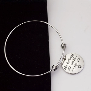 Detailed close-up of adjustable silver bangle with 'she believed' engraved charm