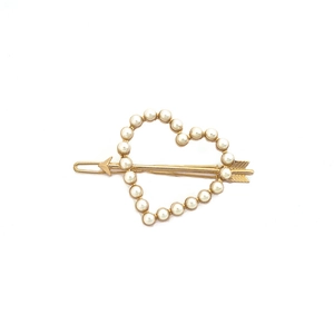 Barrette à cheveux cœur doré avec perles et flèche sur un fond blanc épuré