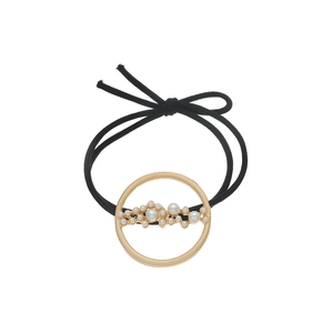 Detail of a minimalist black hair tie with a gold circular frame and inset white pearls