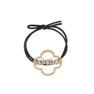 Detail of clover metal charm with white pearls on a black elastic hair tie