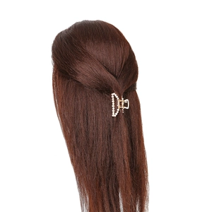 Détail d'une pince à cheveux dorée avec perles blanches sur cheveux bruns ondulés
