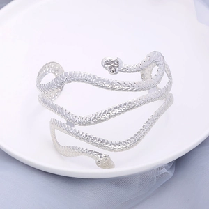Silver snake-shaped wrap arm cuff with detailed scale texture on white ceramic tray