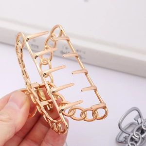 Large golden metal hair claw clip with hollow chain design held in hand for hair styling