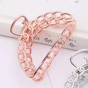 Detailed close-up of large rose gold and silver chain hair clips on a white book surface
