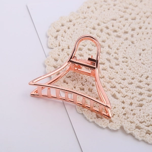 Pince à cheveux triangulaire en métal or rose élégante posée sur de la dentelle blanche
