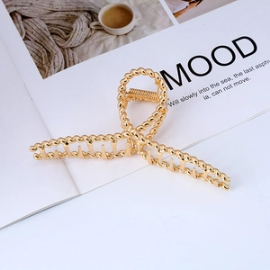 Elegant large golden twisted metal hair claw clip displayed on a minimalist magazine background