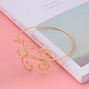 Golden ethnic spiral cuff bracelet featuring intricate filigree design on a pastel background