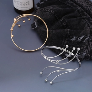 Dettaglio di bracciali rigidi a strati oro e argento con perline su sfondo denim scuro