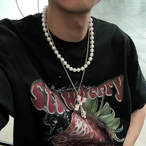 Detailed view of layered white pearl necklace and gold cross pendant on a black shirt