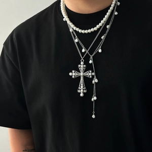 Détail de colliers de perles superposés avec pendentif croix argent sur t-shirt noir