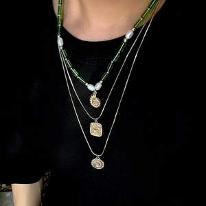 Gros plan sur collier triple rang avec perles vertes et pendentif coquillage doré