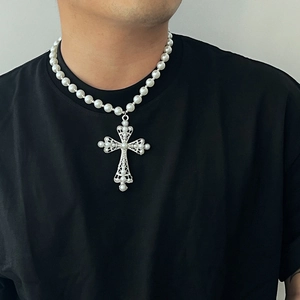 Vue macro d'un grand pendentif croix creuse argentée avec perles sur un collier