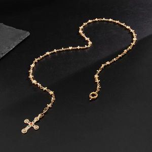 Detailed macro view of a gold cross pendant with colorful gemstones on a star-link chain