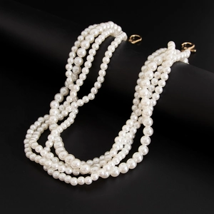 Detail of multilayer pearl chain with golden carabiners on a black stand