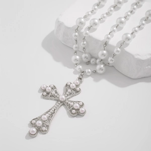 Macro shot of silver filigree cross pendant with inlaid pearls on a white stone background