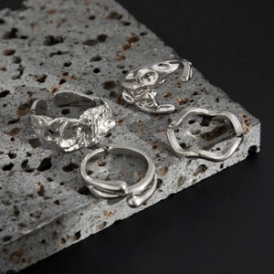 Set mit vier silbernen strukturierten Ringen im Liquid-Metal-Design auf dunklem Lavagestein