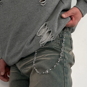 Close-up of punk style trousers chain featuring metallic spider links and silver beads