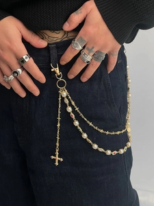 Detail view of a multi-layer gold pant chain with pearls and cross pendant on jeans