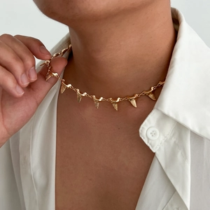 Close-up of golden shark tooth necklace with interlocking metal charms on white shirt
