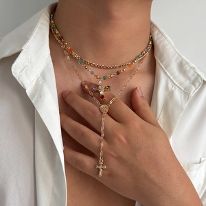 Dettaglio di collane a strati dorate con croci e perline colorate su camicia
