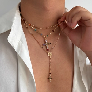 Dettaglio della collana a strati dorata con croce di strass colorati su camicia bianca