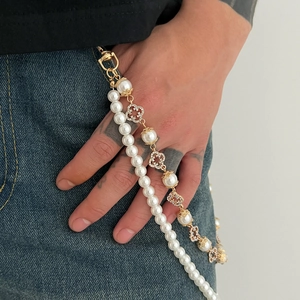 Close-up of hip hop pearl pant chain featuring diamond-encrusted clover pendants on denim