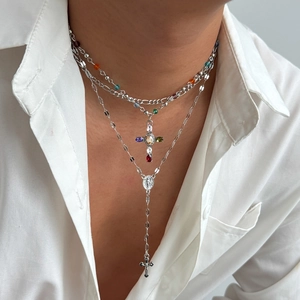 Primo piano di collane a croce in argento a strati con strass colorati su camicia bianca