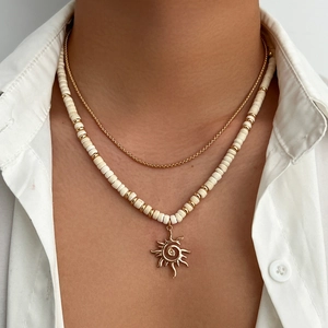 Detail of layered coconut shell bead necklace with a gold sun pendant on white shirt