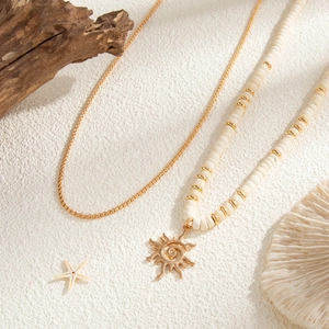 Close-up of coconut shell beaded necklace with golden sun pendant on white sand beach