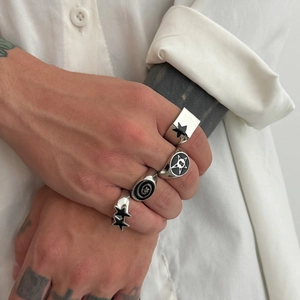 Dettaglio di quattro anelli punk d'argento con stelle smaltate nere su mano tatuata