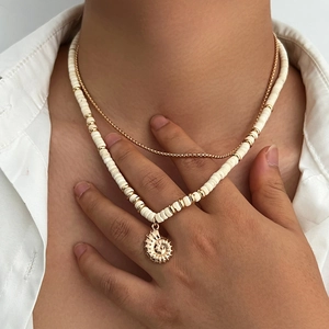 Detail of layered gold chain and white beaded necklace with golden conch shell pendant